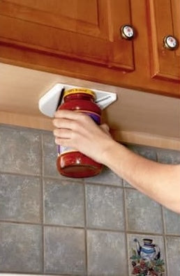 Hand securing a jar in a white vise mounted under a wooden kitchen cabinet, designed to help open stubborn jar lids easily, featured in Kitchen Gadgets and Accessories collections.