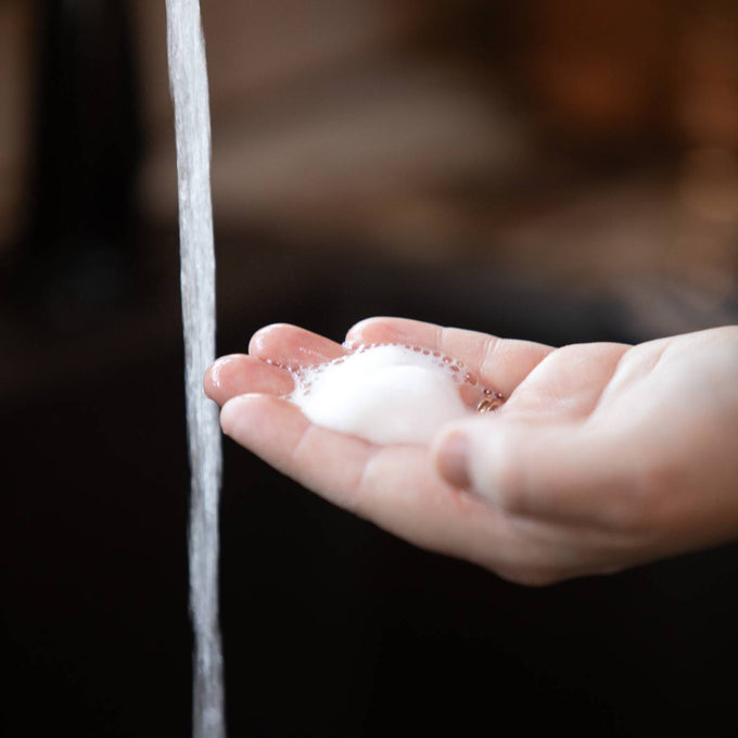 Hand holding rich foam from Lehman's handcrafted moisturizing foaming soap beneath running water, highlighting gentle cleansing in Health & Wellness and Grooming collections.