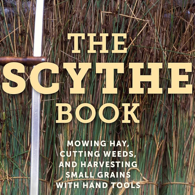 Close-up of the cover of The Scythe Book featuring a tall, handcrafted scythe handle with blade against a backdrop of standing grass, ideal for farm, garden & tool, lawncare, and home and garden how-to books collections.