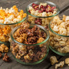 Four clear glass bowls filled with assorted handcrafted popcorn flavors featuring sweet and savory varieties, displayed on a rustic wooden surface, part of Kitchen & Food, Snacks and Sweets, Popcorn, USA Made, Best Sellers, and Promo Eligible collections.