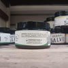 Small black jar of natural muscle balm with a white label listing coconut oil, cocoa butter, beeswax, and essential oils, part of Health & Wellness, Balms, Creams and Lotions, USA Made, and Best Sellers collections.