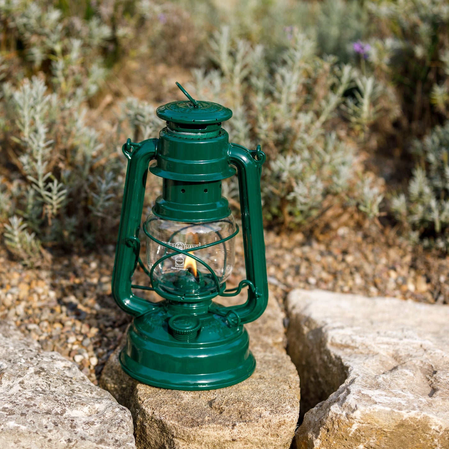 Handcrafted green galvanized oil lantern with thermal heat-resistant SUPRAX globe, glowing gently while resting on a stone surface outdoors, ideal for Lamps & Lighting, Camping, and Emergency Supplies collections.