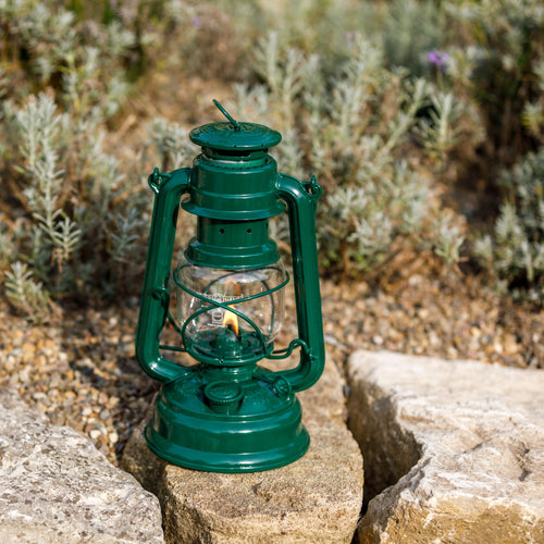 Handcrafted green galvanized oil lantern with thermal heat-resistant SUPRAX globe, glowing gently while resting on a stone surface outdoors, ideal for Lamps & Lighting, Camping, and Emergency Supplies collections.