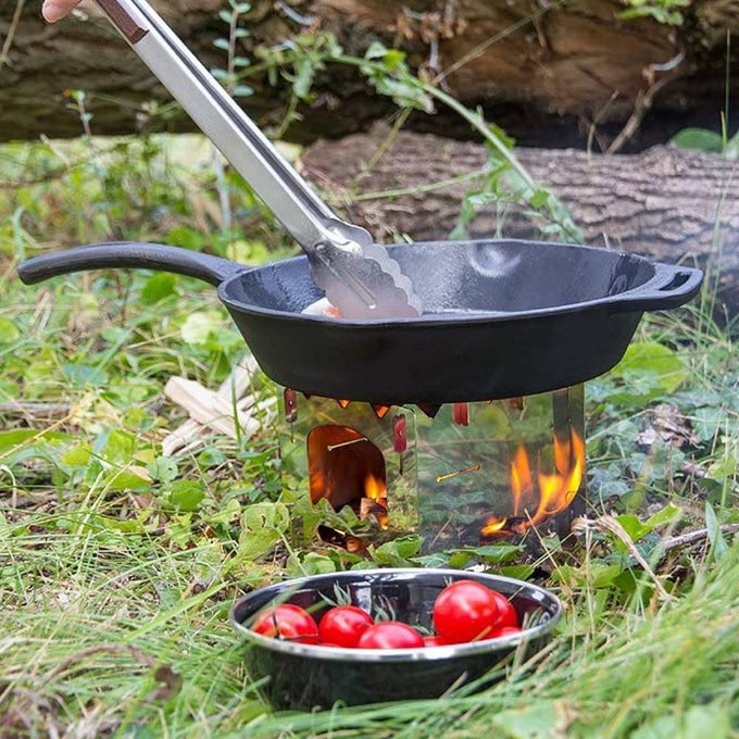 Cast iron skillet with long handle cooking over an open flame on a portable stove in a grassy outdoor setting, accompanied by a bowl of fresh cherry tomatoes, featured in Farm, Garden & Tool, Camping, Kitchen & Food, Cookware, Cast Iron, and Best Sellers collections.