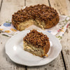 Slice of homemade pecan roll topped with chopped nuts and caramel glaze, handcrafted in the USA, displayed on a white plate with the full roll in the background on rustic wood.