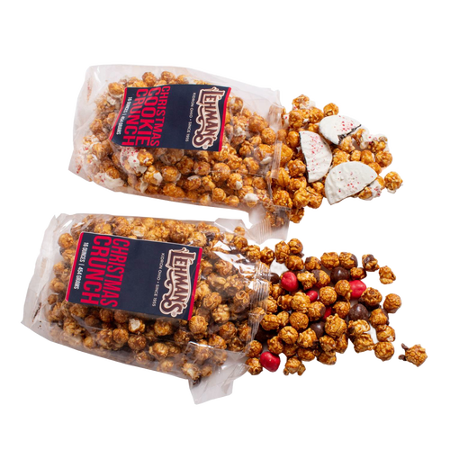 Two clear bags of handcrafted caramel popcorn with holiday-themed additions spilling out, including white chocolate peppermint bark pieces and red candy, for Kitchen & Food, Snacks and Sweets, Popcorn, and Best Sellers collections.