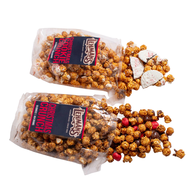 Two clear bags of handcrafted caramel popcorn with holiday-themed additions spilling out, including white chocolate peppermint bark pieces and red candy, for Kitchen & Food, Snacks and Sweets, Popcorn, and Best Sellers collections.