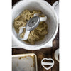 Close-up of thick cookie dough being mixed in a white bowl by dual cookie paddle attachments, accompanied by a heart-shaped cookie cutter on a wooden surface, USA Made kitchen gadget.
