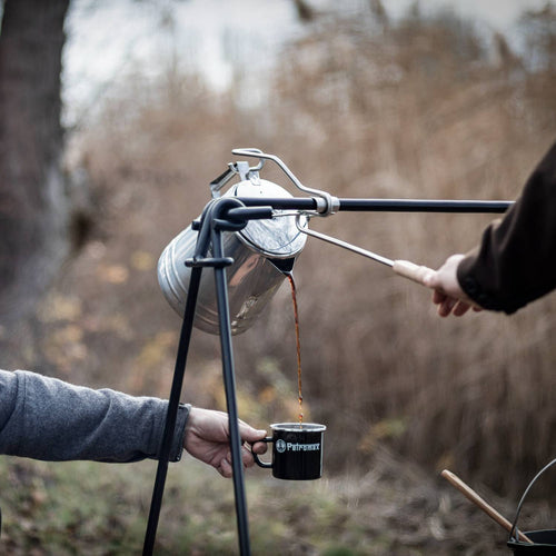 Pouring hot coffee from a campfire percolator using a metal pouring aid with wooden handle, held over a black enamel mug outdoors, ideal for Farm, Garden & Tool, Camping, and Best Sellers collections.