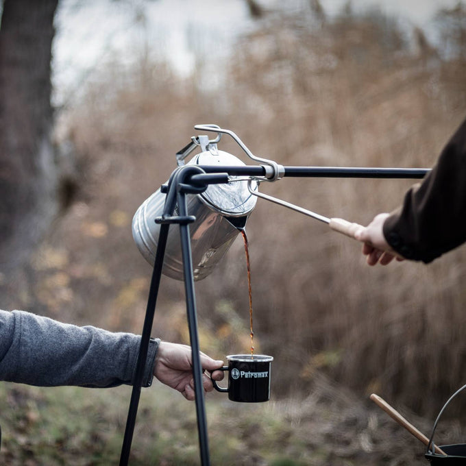 Pouring hot coffee from a campfire percolator using a metal pouring aid with wooden handle, held over a black enamel mug outdoors, ideal for Farm, Garden & Tool, Camping, and Best Sellers collections.