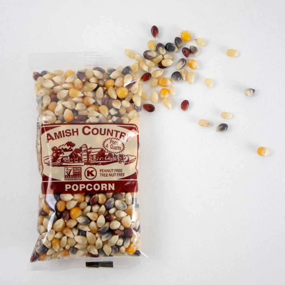 Clear plastic bag of multicolored Amish Country popcorn kernels spilling onto a white surface, highlighting handcrafted, USA made popcorn in Kitchen & Food and Snacks collections.