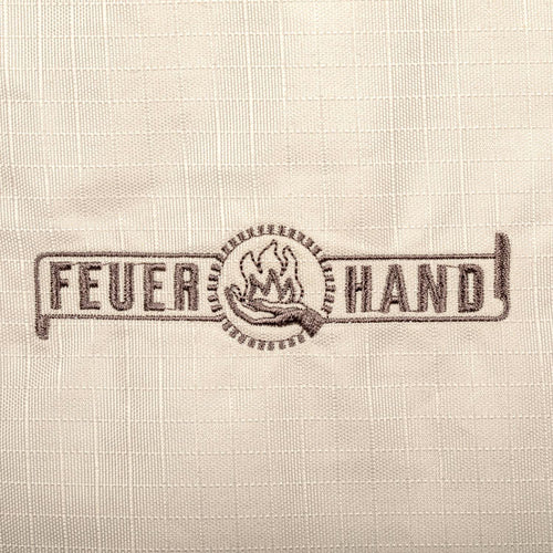 Close-up of the Feuerhand logo embroidered on weather-resistant ripstop fabric in light beige, featured in Farm, Garden & Tool and Camping collections.