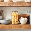 Clear glass jar with airtight lid filled with dried pasta nests, displayed on a rustic wooden kitchen shelf alongside bowls, a whisk, a ceramic bowl with garlic, and a bottle, suitable for Home & Decor, Kitchen & Food, and Storage collections.