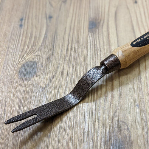 Handcrafted grubber weeding tool featuring a powder-coated, hammer-finished steel fork and smooth natural wood handle with leather loop, ideal for farm, garden, and lawncare use.