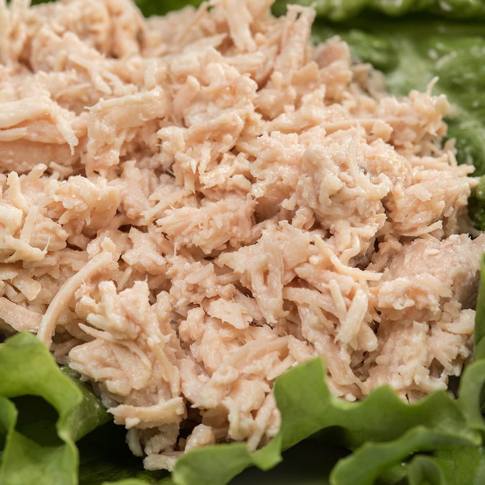 Close-up of shredded canned turkey meat on fresh green lettuce leaves, highlighting a convenient, long-lasting protein option ideal for emergency supplies, kitchen and food collections.