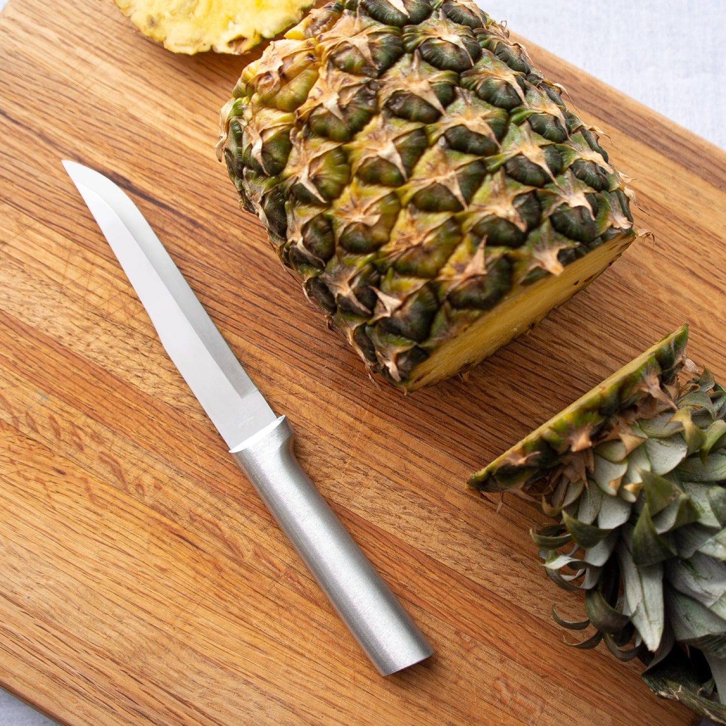 Handcrafted Rada Stubby Butcher Knife with a 5-3/8" stainless steel blade and silver brushed aluminum handle, shown cutting a fresh pineapple on a wooden board, ideal for Kitchen & Food and Food Prep collections.