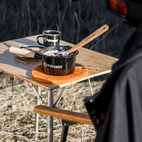 Black enamel pan with wooden handle cooking oatmeal with raisins on a foldable wooden outdoor table, accompanied by matching enamel mug, ideal for camping and outdoor use in Farm, Garden & Tool, Kitchen & Food, Camping, Cookware, Pots and Pans, Best Sellers, Promo Eligible collections.
