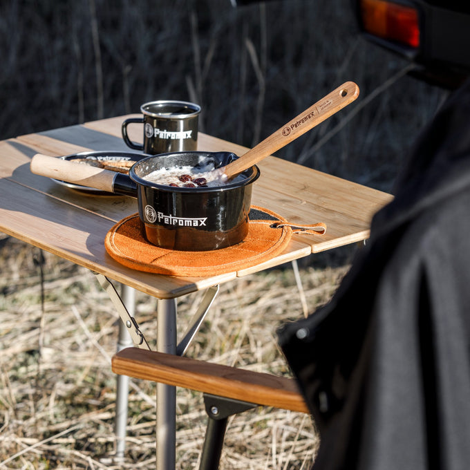 Black enamel pan with wooden handle cooking oatmeal with raisins on a foldable wooden outdoor table, accompanied by matching enamel mug, ideal for camping and outdoor use in Farm, Garden & Tool, Kitchen & Food, Camping, Cookware, Pots and Pans, Best Sellers, Promo Eligible collections.