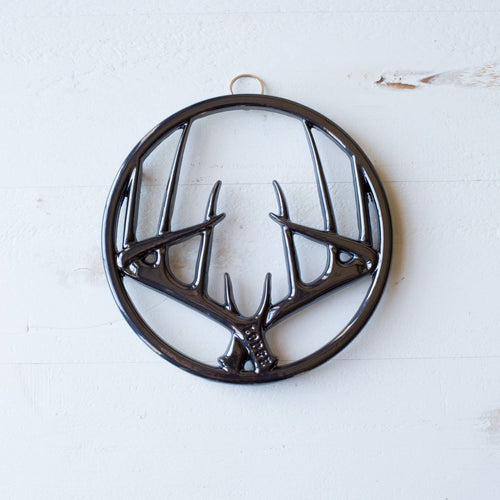 Glossy black enamel trivet with antler motif in a circular frame, featuring built-in hanger and rubber feet, perfect for Kitchen & Food, Dinnerware, Storage and Serving, Best Sellers, and Promo Eligible collections.