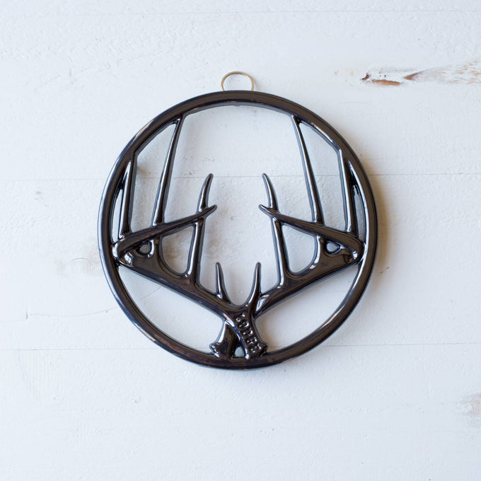 Glossy black enamel trivet with antler motif in a circular frame, featuring built-in hanger and rubber feet, perfect for Kitchen & Food, Dinnerware, Storage and Serving, Best Sellers, and Promo Eligible collections.