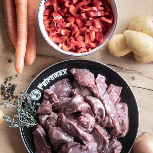 Black enamel outdoor plate with Petromax logo holding raw meat, surrounded by chopped red bell peppers in a white bowl, carrots, potatoes, onion, and fresh herbs, ideal for camping and outdoor cooking in Farm, Garden & Tool, Kitchen & Food, Camping, Dinnerware, Best Sellers, and Promo Eligible collections.