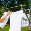 Hands hanging white clothes on a large deluxe rotating outdoor clothes dryer in a green yard, part of Home & Decor, Laundry Supplies, and Clothesline Accessories collections.