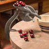 Handcrafted antique-style cherry pitter made in USA with durable cast body and crank wheel, shown with fresh cherries on a kitchen table, ideal for Kitchen & Food and Specialty Equipment collections.