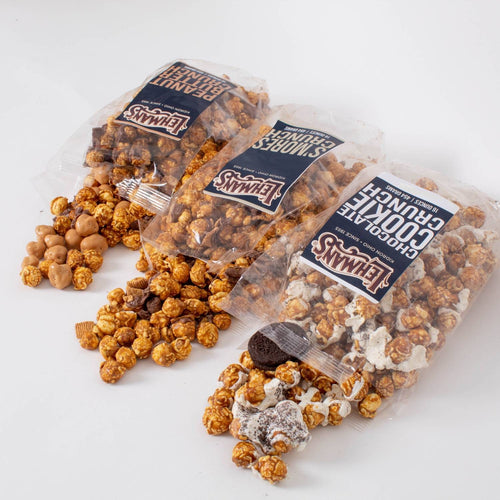 Three clear bags of handcrafted caramel popcorn crunch in different flavors including peanut butter, s'mores, and chocolate cookie, a unique sweet and crunchy snack made in USA, ideal for Kitchen & Food, Snacks and Sweets, Popcorn, USA Made, Best Sellers, and Promo Eligible collections.