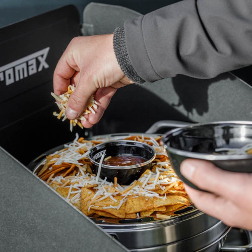 Close-up of a hand sprinkling shredded cheese over a tray of nachos with a central dip container inside a handcrafted mini camping oven, featured in Farm, Garden & Tool, Camping, Best Sellers, and Promo Eligible collections.