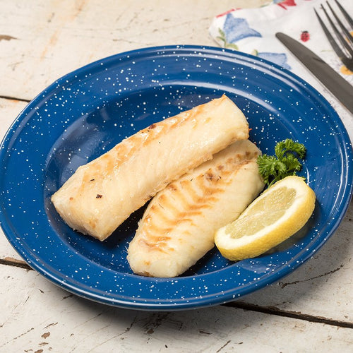 Cooked fillets of white fish arranged on a blue speckled plate with a lemon wedge and fresh parsley, set on a rustic wooden surface with a fork and knife nearby.