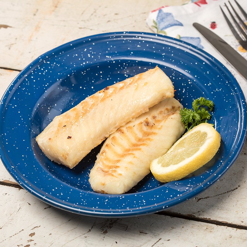 Cooked fillets of white fish arranged on a blue speckled plate with a lemon wedge and fresh parsley, set on a rustic wooden surface with a fork and knife nearby.