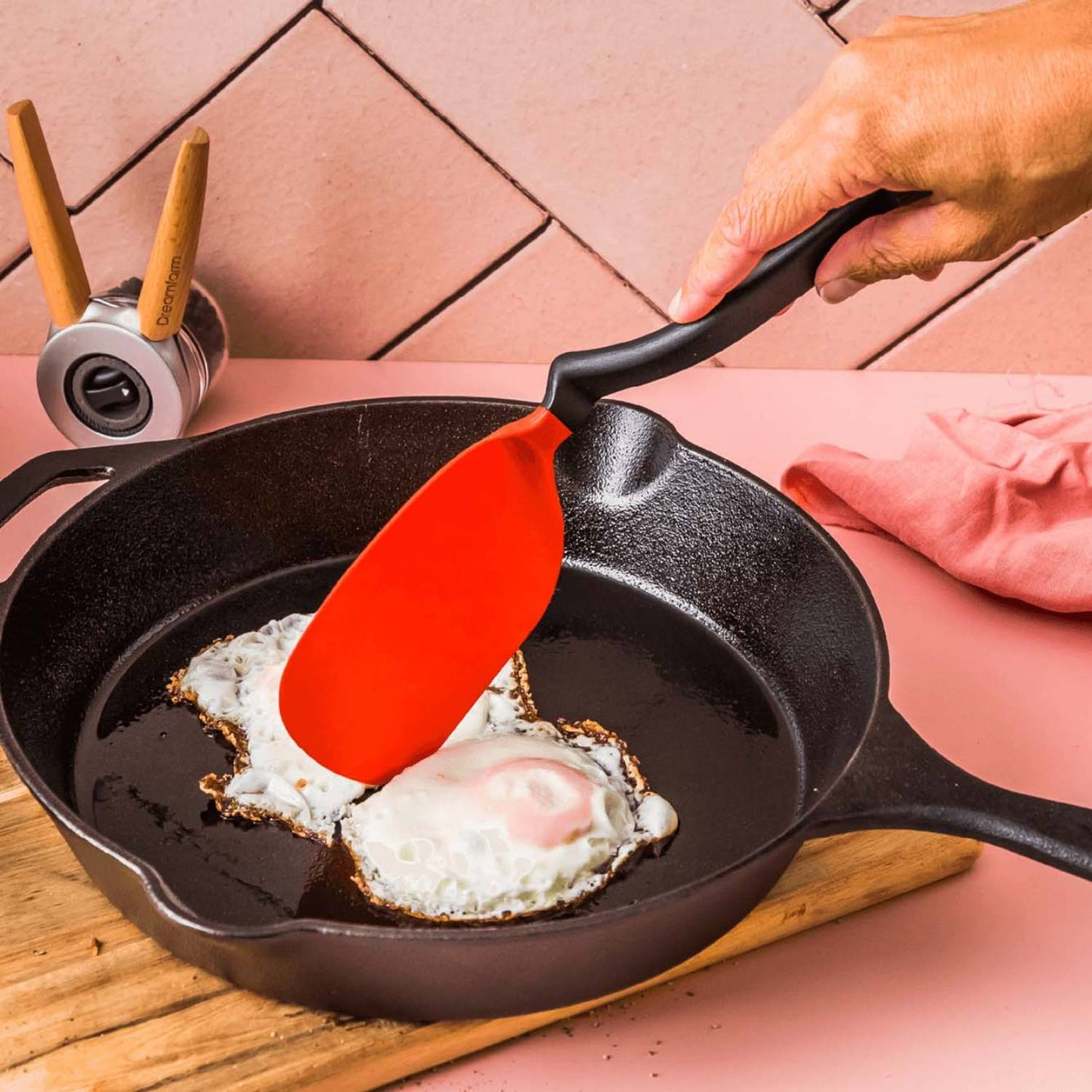 Hand using a flexible red spatula to lift a fried egg from a cast iron skillet on a wooden board, featured in Kitchen & Food, Kitchen Gadgets, Cooking and Baking Helpers, Best Sellers, and Promo Eligible collections.