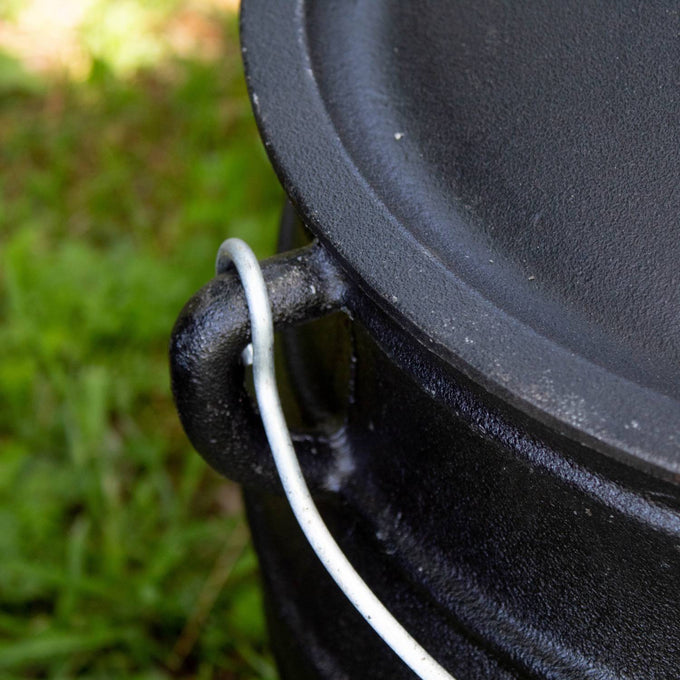 Close-up of a handcrafted cast iron campfire kettle lid and sturdy bail handle resting on green grass, perfect for Farm, Garden & Tool, Camping, Best Sellers, and Promo Eligible collections.