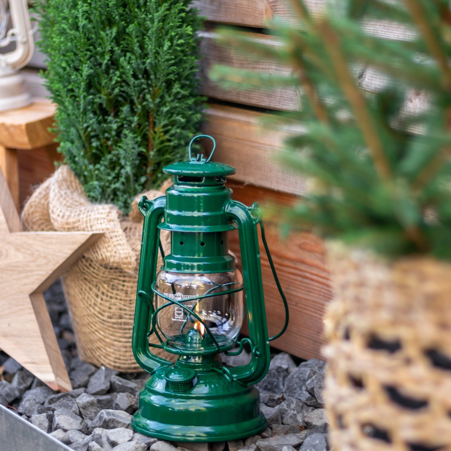 Handcrafted green galvanized oil lantern with thermal heat-resistant globe softly glowing among rustic wooden decor and greenery, perfect for Lamps & Lighting, Camping, and Emergency Supplies.