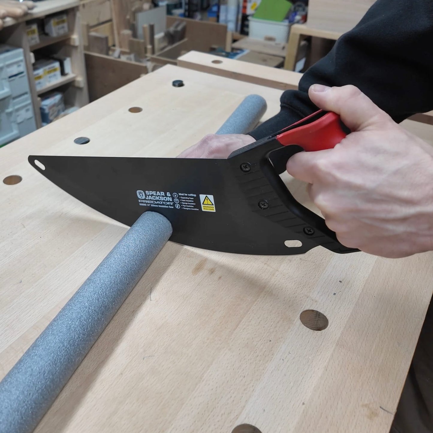 Hand tool with carbon steel curved blade and ergonomic black and red handle cutting gray foam pipe insulation on wooden workbench, featured in Farm, Garden & Tool and Best Sellers collections.