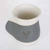 Handcrafted 16 oz ceramic mug in gray and white with a reactive glaze, featuring a recessed handwarmer pocket and an embossed stag design, ideal for Kitchen & Food and Dinnerware collections.