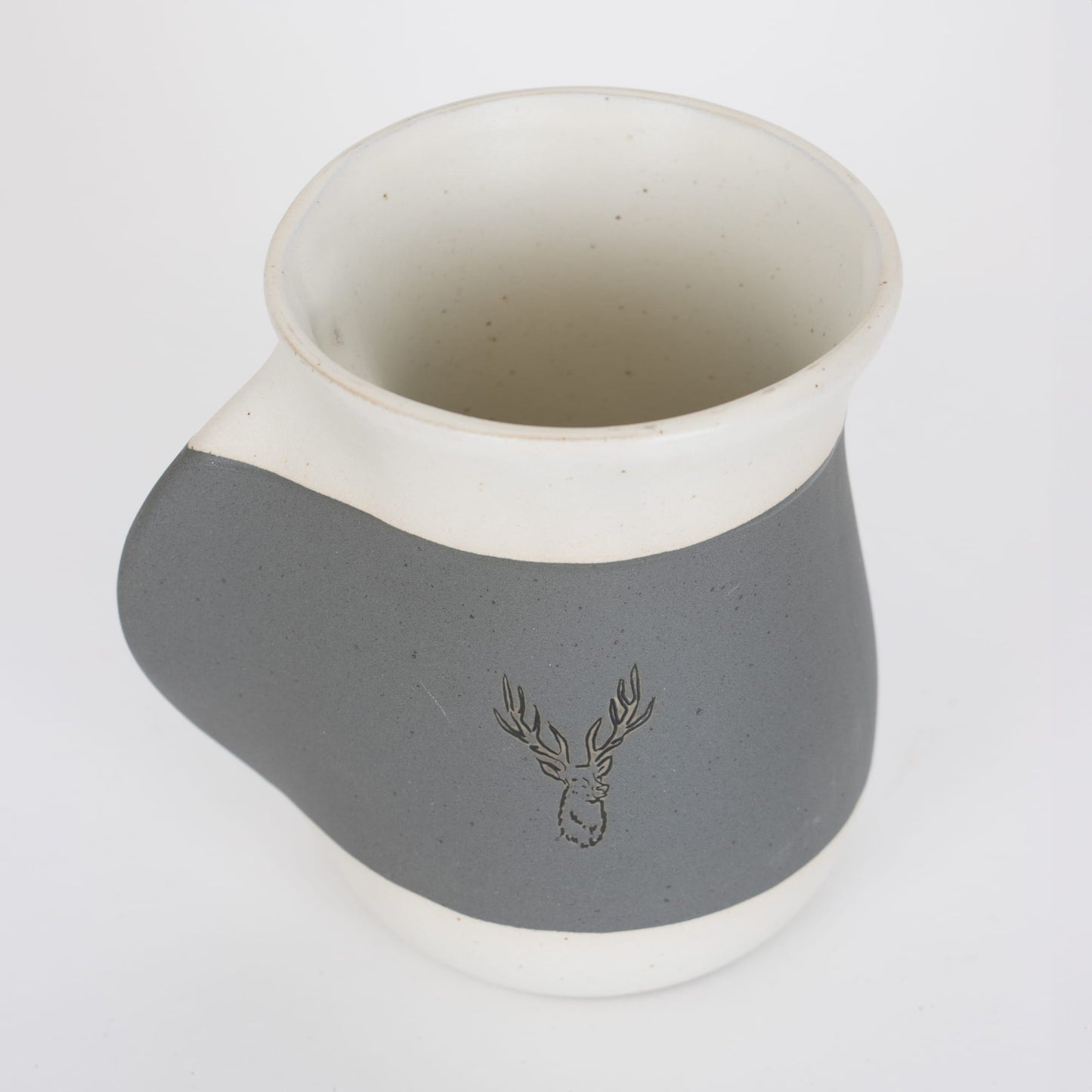 Handcrafted 16 oz ceramic mug in gray and white with a reactive glaze, featuring a recessed handwarmer pocket and an embossed stag design, ideal for Kitchen & Food and Dinnerware collections.