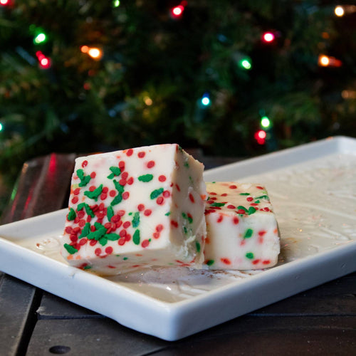 Two handcrafted creamy white fudge squares with festive red and green sprinkles on a white rectangular plate, featured in Kitchen & Food, Snacks and Sweets, USA Made, and Best Sellers collections.