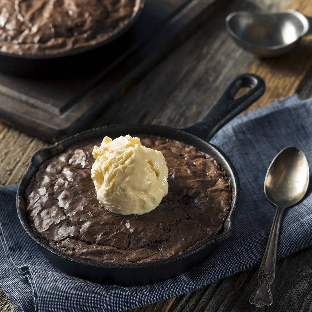 Handcrafted ooey gooey brownie baked in a 6-inch cast iron skillet topped with a scoop of vanilla ice cream, styled with vintage spoon on rustic cloth in Kitchen & Food, Dry Goods and Mixes collections.