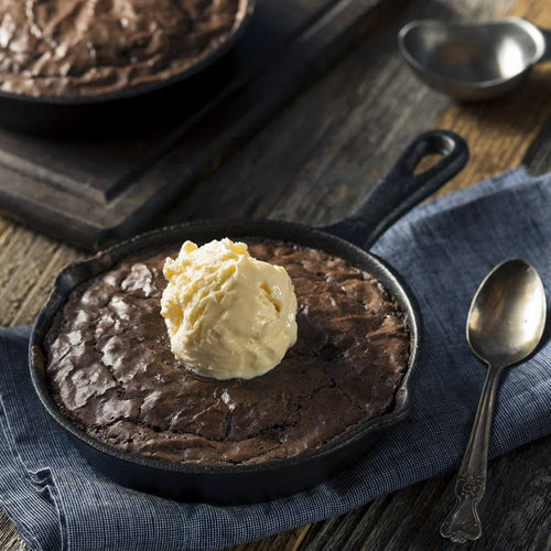 Handcrafted ooey gooey brownie baked in a 6-inch cast iron skillet topped with a scoop of vanilla ice cream, styled with vintage spoon on rustic cloth in Kitchen & Food, Dry Goods and Mixes collections.