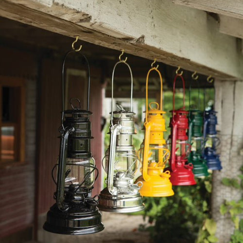 Row of colorful vintage-style metal lanterns in black, silver, yellow, red, green, and blue hanging from rustic wooden ceiling hooks, fitting Lamps & Lighting and Promo Eligible collections.