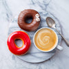 Round polished marble tray with smooth surface, holding a cup of frothy coffee, a silver spoon, and two colorful glazed donuts, ideal for stylish kitchen and dining settings.
