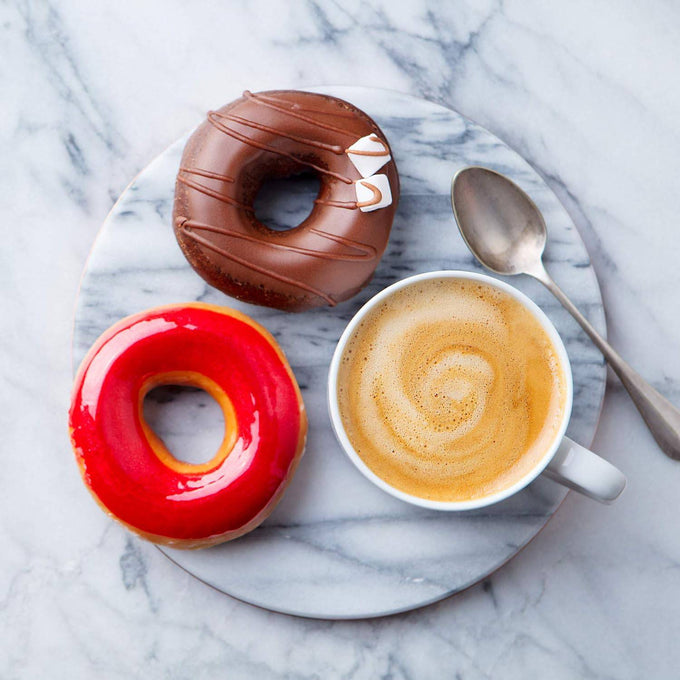 Round polished marble tray with smooth surface, holding a cup of frothy coffee, a silver spoon, and two colorful glazed donuts, ideal for stylish kitchen and dining settings.