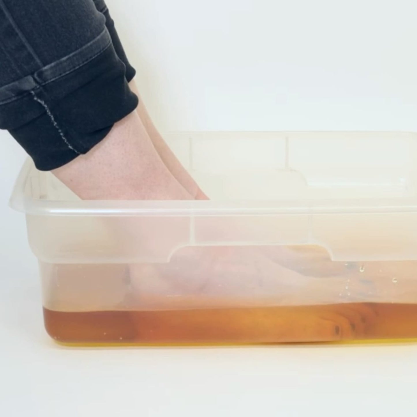 Feet soaking in a clear plastic basin filled with warm herbal solution, demonstrating a natural remedy for nail and skin health in Health & Wellness and USA Made collections.