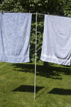 Lightweight steel clothesline prop with plastic end cap supporting a taut clothesline holding large towels outdoors, ideal for Home & Decor and Laundry Supplies collections.