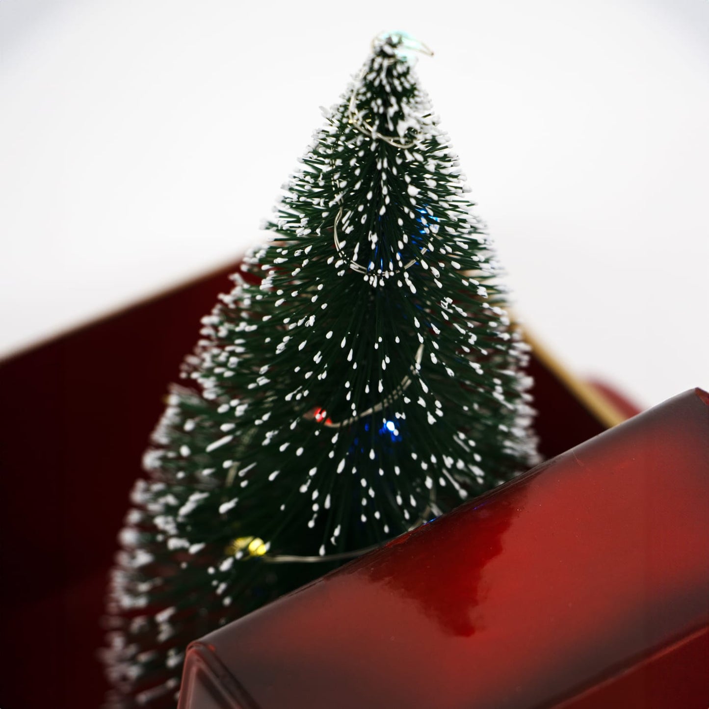 Close-up of handcrafted lighted green holiday tree with white frosted tips and tiny colorful lights, featured in Home & Decor, Holiday Decor, and Best Sellers collections.