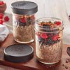 Two wide mouth glass jars filled with overnight oats topped with fresh blackberries, raspberries, and granola, one sealed with a textured dark gray leak-proof lid, set on a wooden board, ideal for Kitchen & Food and Storage and Serving collections.