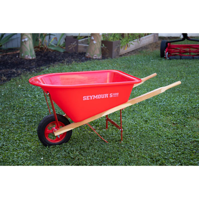 Child’s wheelbarrow with solid wood handles, durable red poly bed, metal frame, and rubber tire set outdoors on grass, handcrafted for Toys, Books & Games and Lawn Games collections.