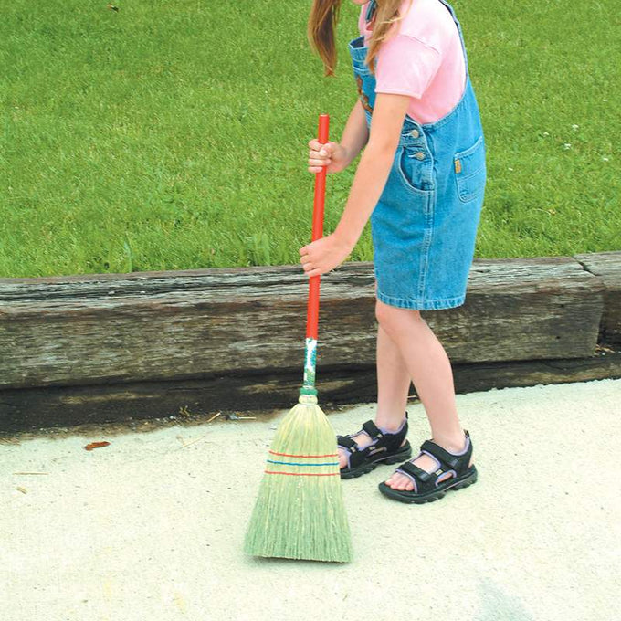 Child holding a handcrafted small corn straw broom with a red handle, designed for outdoor play and household cleaning, made in the USA and Amish made, featured in children's toys and home decor.