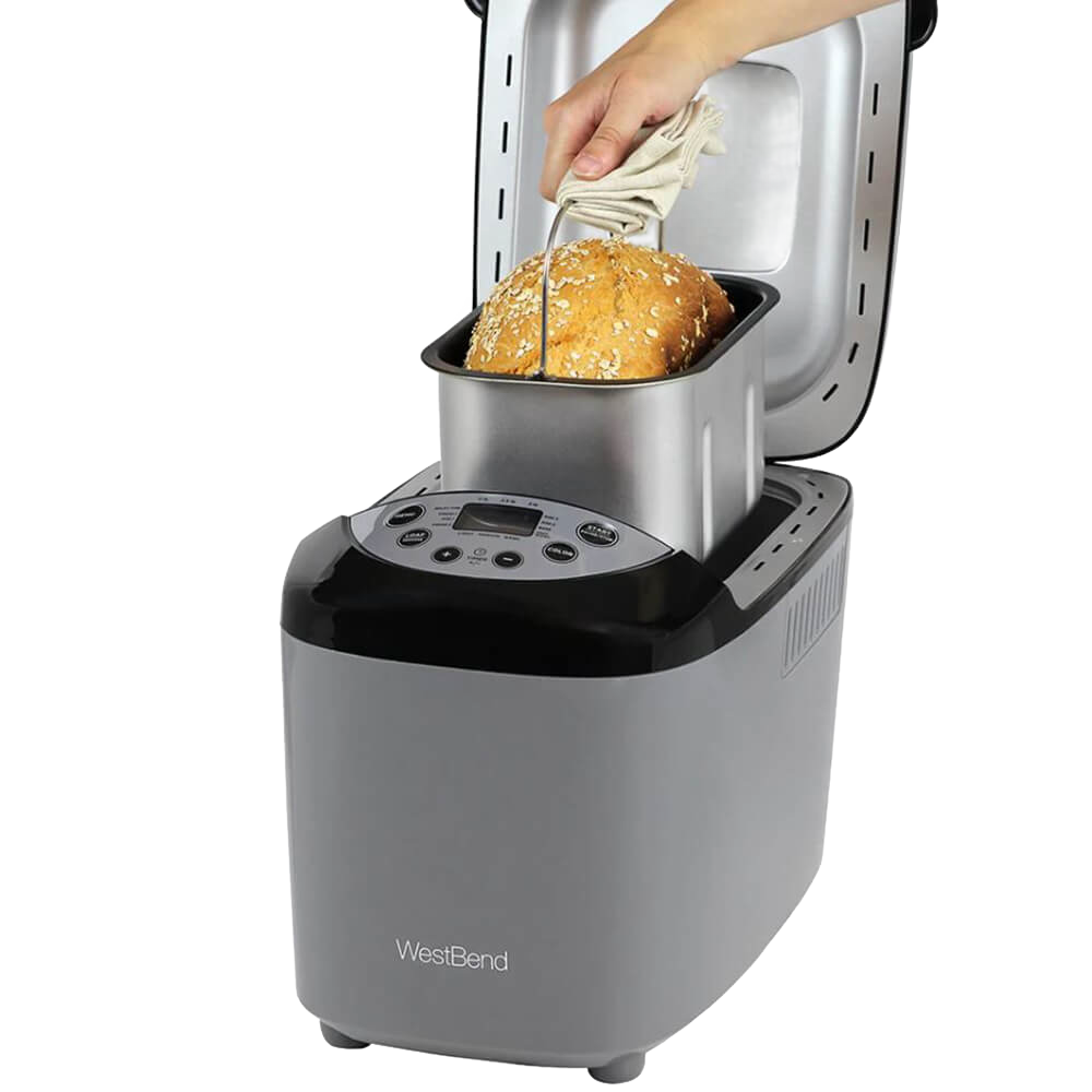 Hand removing freshly baked multigrain bread from a silver and black electric bread maker machine with digital controls, ideal for Kitchen & Food and Bread Making Supplies collections.